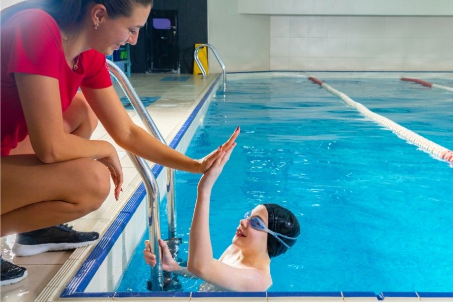 Schwimmtrainerin klatsch mit einem Schüler ab, der in Frankfurt Schwimmen gelernt hat